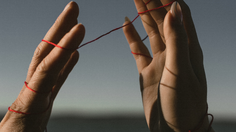 Two hands holding red thread symbolizing connection in couples counseling, Port Charlotte.
