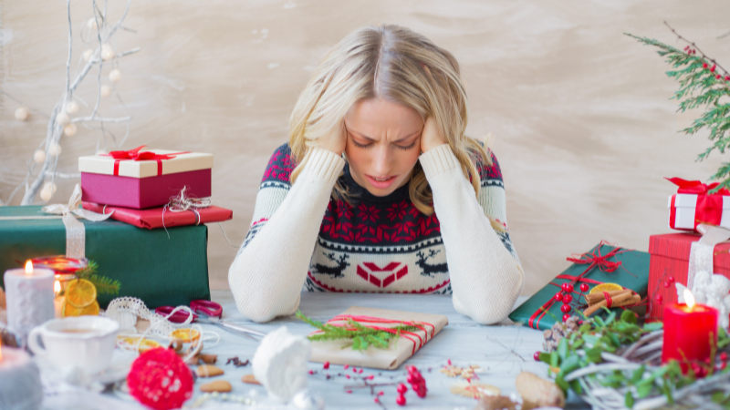 Stressed woman surrounded by Christmas gifts and decorations, looking overwhelmed, illustrating the need for North Port therapists during the holidays.