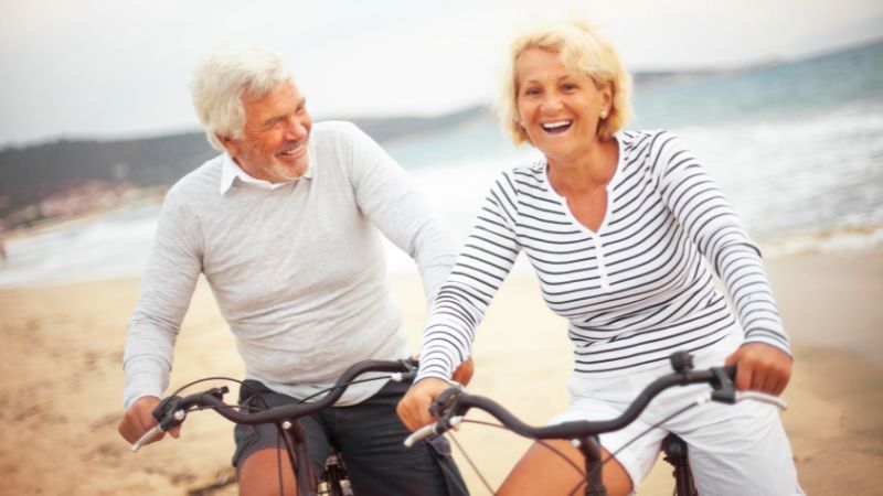 Happy couple in casual attire riding bikes on a beach in North Port, embodying active living and companionship.